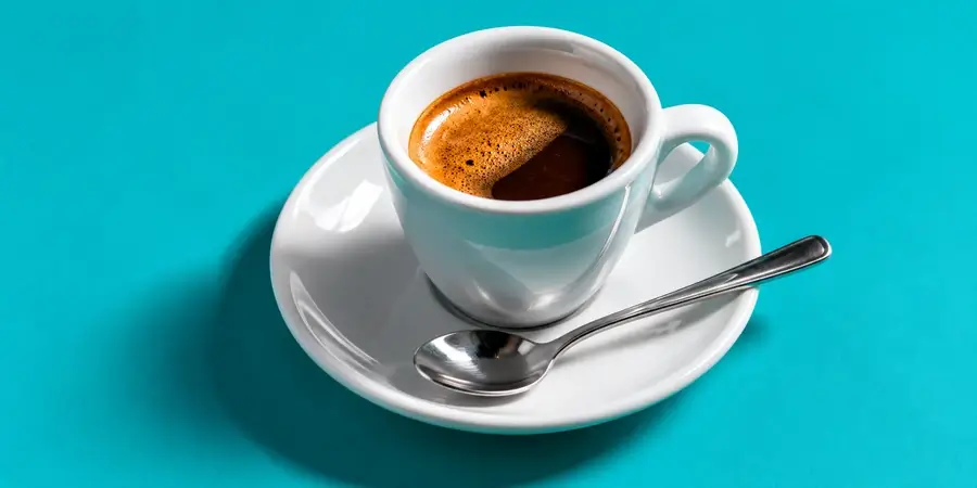 Tazzina di espresso nero con il cucchiaino pulito sul piattino su fondo turchese